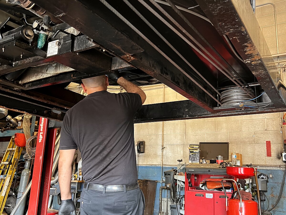 An AutoMax technician working beneath a vehicle on the lift during brake and exhaust service
