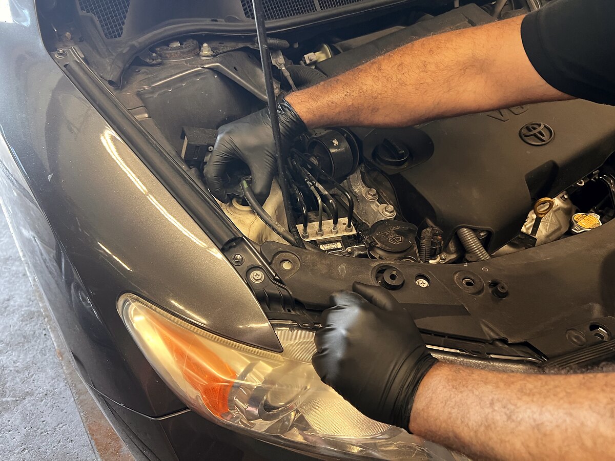 A gloved AutoMax technician servicing the engine bay of a Toyota in the shop