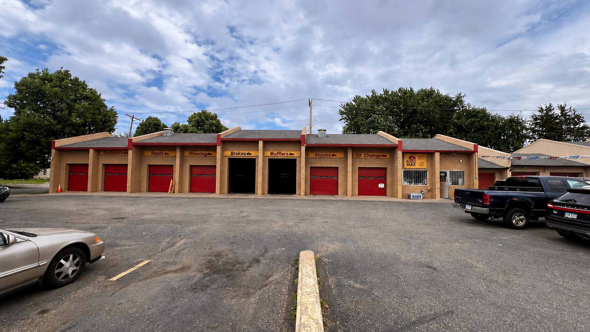 The AutoMax Complete Auto Service shop on University Ave W in Saint Paul — a long row of red service-bay doors under a dramatic sky